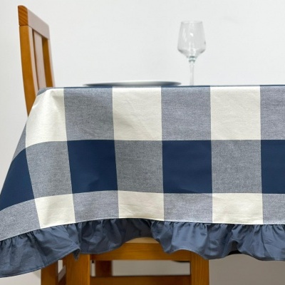 toalha de mesa xadrez azul e branca com folhos azuis numa mesa de madeira com copo de vidro