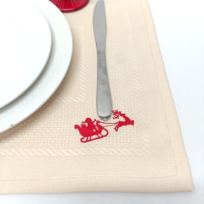 Lugar americano bege com bordado vermelho de trenó e rena, faca e pratos brancos
