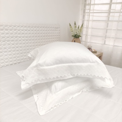 Pillowcases brancos com bordado e canto recortado sobre cama branca em quarto iluminado