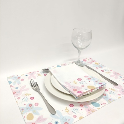 Conjunto de loiça com pratos brancos, guardanapo e individual com padrão floral, talheres metálicos e copo de vidro