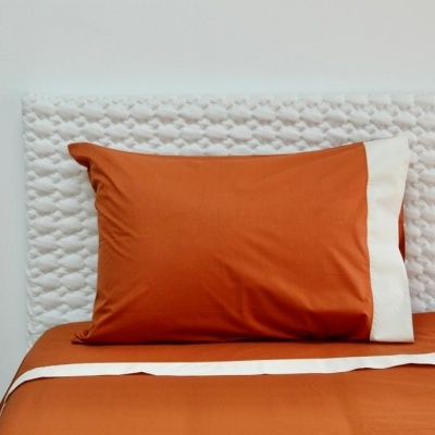 Travesseiro com fronha laranja e branca numa cama com lençol laranja e cabeceira branca texturada