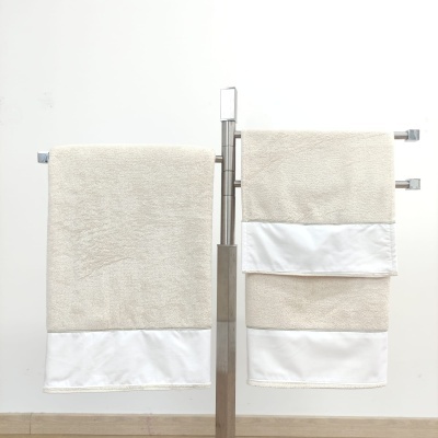 Toalheiros bege com faixa branca pendurados num suporte metálico