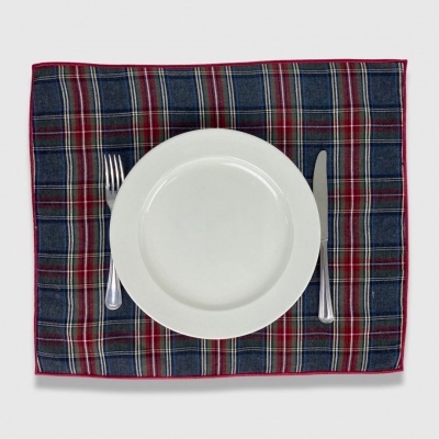 Mesa posta com guardanapo xadrez azul e vermelho, prato branco, garfo e faca metálicos