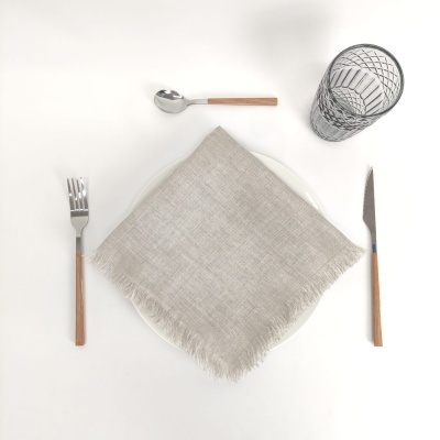 Conjunto de talheres com cabo de madeira, copo de vidro com padrão geométrico, prato branco e guardanapo cinza claro sobre mesa branca