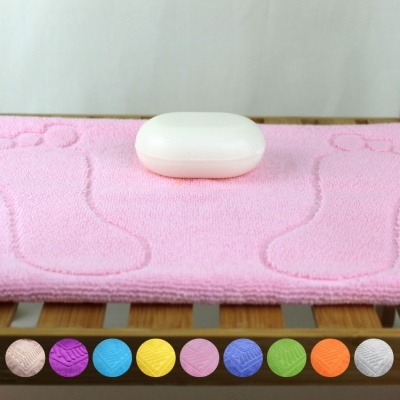 Tapete de banho rosa com pegadas e estojo branco sobre madeira