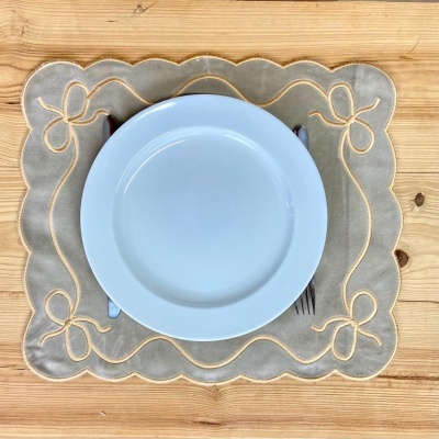 Conjunto de mesa com prato branco em cima de guardanapo bege bordado numa mesa de madeira