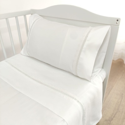 Cama infantil com roupa de cama branca e detalhes bordados