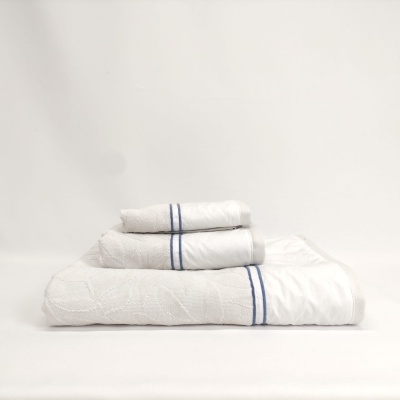 Conjunto de três toalhas brancas com faixas azuis empilhadas sobre superfície branca.