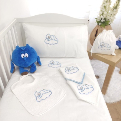 Conjunto de roupa de cama e acessórios para bebé com bordados azuis e peluche azul num berço branco