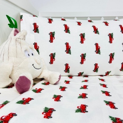Cama infantil com lençóis brancos de carrinhos vermelhos com árvores de Natal e peluche em forma de tronco