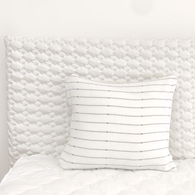 Almofada branca com riscas finas pretas sobre cama com cabeceira branca acolchoada