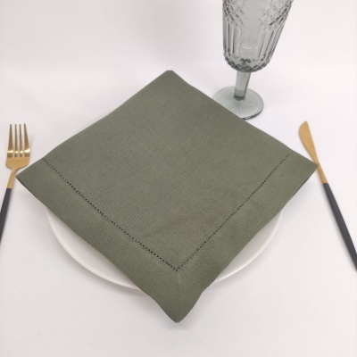 Guardanapo de tecido verde sobre prato branco com talheres dourados e copo de vidro