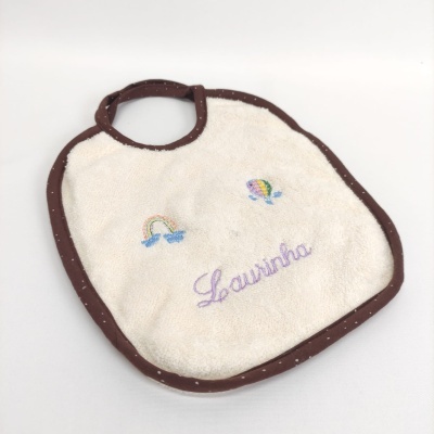 Babete de bebé branco com bordas castanhas, bordados e nome Laurinha.