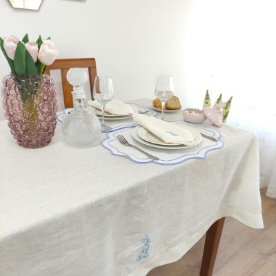 Mesa posta com toalha de linho, pratos brancos, copos e jarra de vidro, vaso rosa com flores