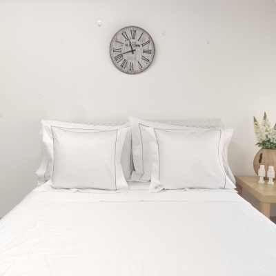 Cama com roupa branca, relógio de parede e mesa de cabeceira