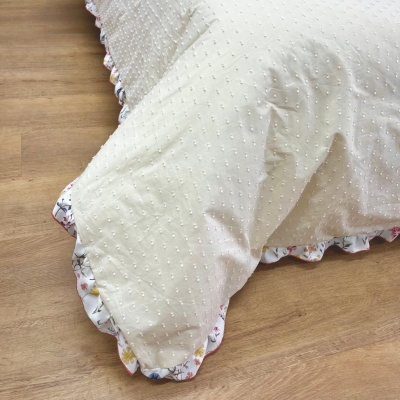 Capa de almofada branca com textura e borda floridada em chão de madeira