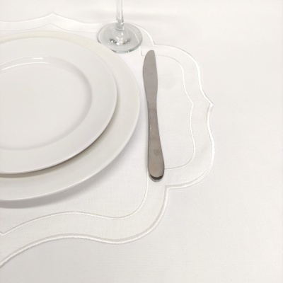 Conjunto de pratos brancos, faca de metal e copo de vidro sobre toalha branca bordada