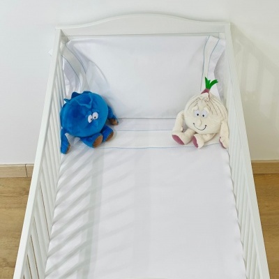 Berço branco com lençol branco e dois peluches, em chão de madeira clara