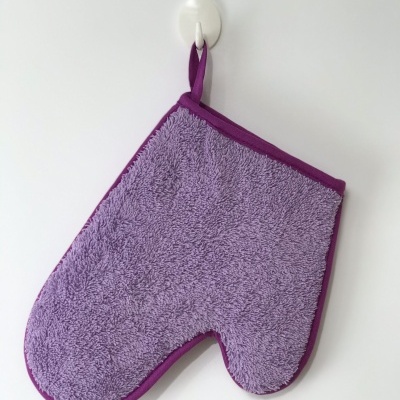 Luvas de cozinha roxas penduradas numa parede branca.