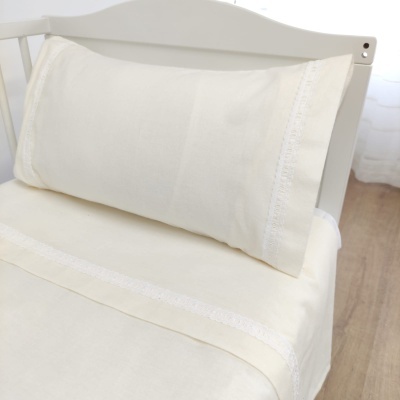 Conjunto de roupa de cama creme com detalhes em renda branca sobre cama branca