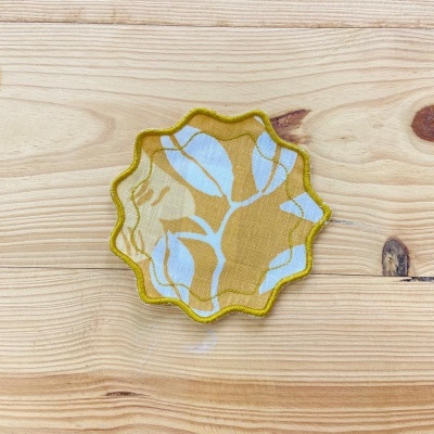 Apoio para copos em tecido com padrão de folhas coloridas sobre madeira clara