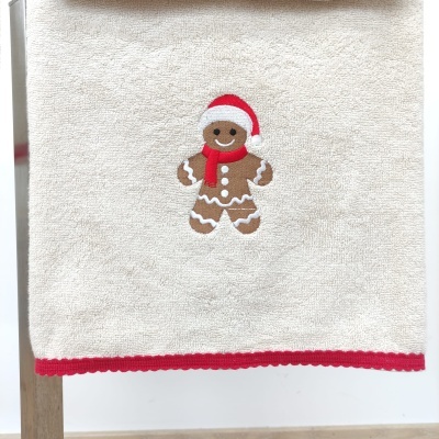 Toalha branca com borda vermelha e bordado de bolo de gengibre com gorro vermelho.
