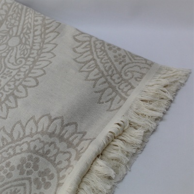 Toalha ou manta bege com padrão decorativo e franjas