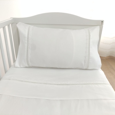 Conjunto de roupa de cama branco com renda numa cama branca.