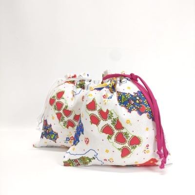 Dois sacos coloridos com padrão de corações e estrelas, com cordões rosa e branco