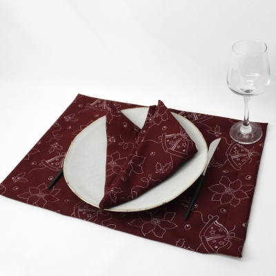 Conjunto de mesa bordô com padrão floral e utensílios, prato branco, copo de vidro e talheres pretos sobre fundo branco.