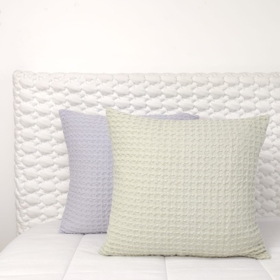 Três almofadas texturizadas claras numa cama com cabeceira branca acolchoada