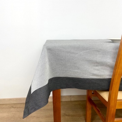 Toalha de mesa cinzenta clara com borda cinzenta escura numa mesa de madeira