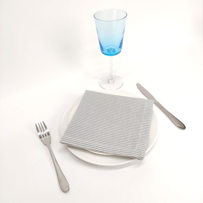 Conjunto de jantar com copo azul, guardanapo cinza e talheres prateados