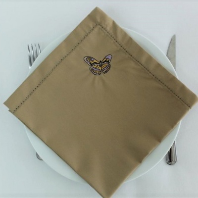 Guardanapo bege com bordado de borboleta sobre prato branco com talheres