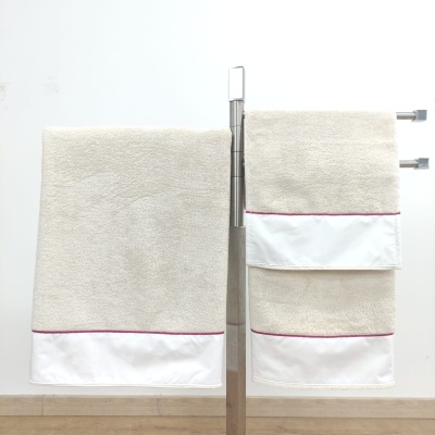 Duas toalhas de mão creme com faixa branca e linha vermelha num suporte metálico