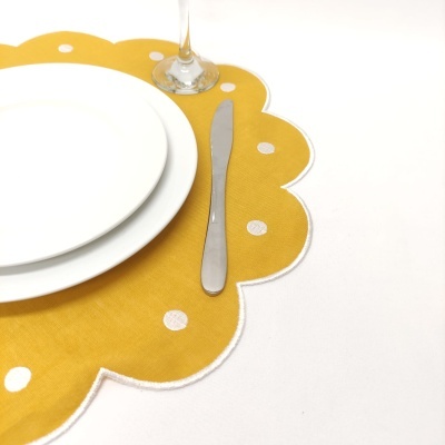 Jogo americano amarelo com pontos brancos e bordas onduladas com pratos, faca e copo