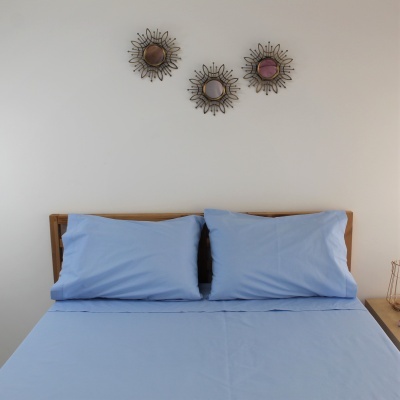 Cama com lençóis azuis claros e espelhos decorativos de metal na parede