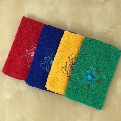 Toalhas de banho coloridas com bordado de flor sobre superfície de madeira.