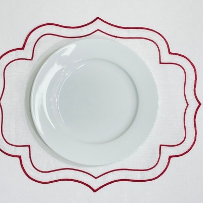 Pratos brancos redondos sobre toalha branca com bordado vermelho.