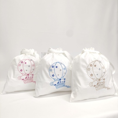 Três sacos de tecido branco com desenhos bordados de balões de ar quente e ovelhas em rosa, azul e bege