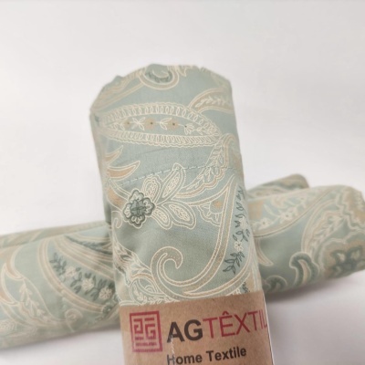 Tecido enrolado com padrão paisley azul e bege com etiqueta AGTÉXTIL Home Textile