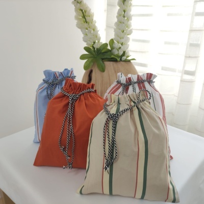 Quatro sacos de tecido coloridos com cordão sobre mesa branca com vaso de madeira e flores