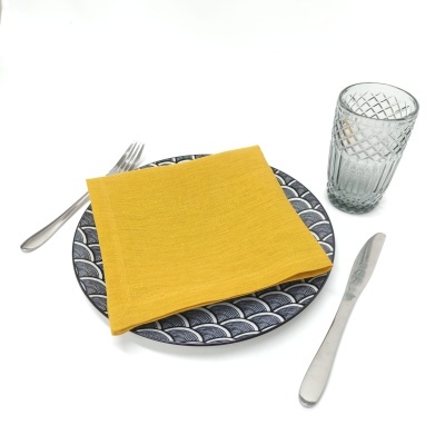 Conjunto de prato azul com guardanapo amarelo, talheres metálicos e copo de vidro texturizado