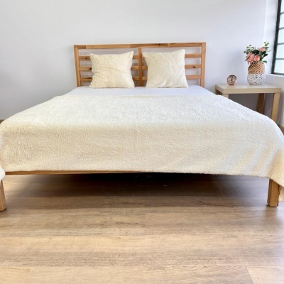 Cama de casal em madeira clara com roupa de cama e almofadas amarelas claras em ambiente minimalista.
