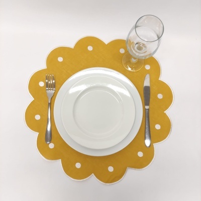 Louça branca sobre individual amarelo com pontos brancos, garfo, faca e copo de vidro