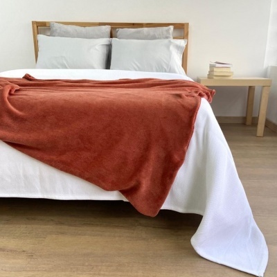 Cama com manta ferrugem sobre lençol branco e cabeceira de madeira clara