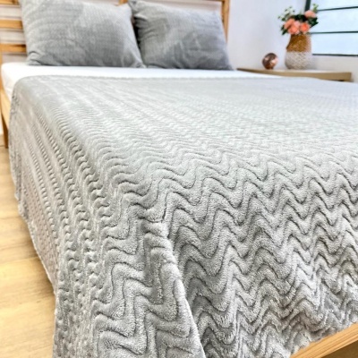 Cobertor cinzento claro com padrão ondulado em relevo numa cama de madeira