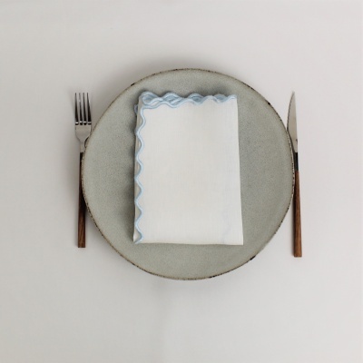 Conjunto de mesa com prato cinza, guardanapo branco com borda azul e talheres com cabo de madeira.