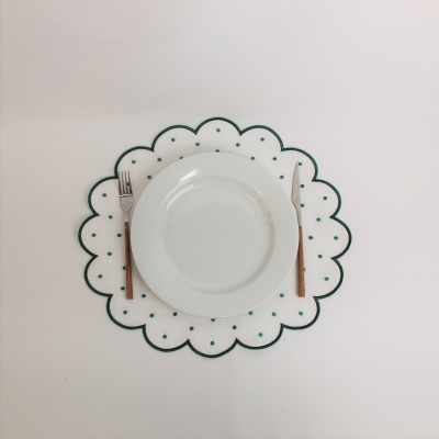 Conjunto de jantar com prato branco sobre individual branco com pontos verdes, garfo e faca com cabos de madeira