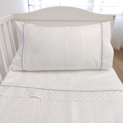 Roupa de cama branca com bordado azul num berço branco